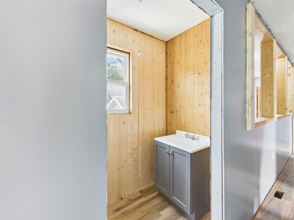 Bathroom with wood-paneled walls, a gray vanity, and a window.