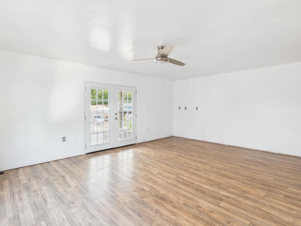 Empty room with wood-look flooring, ceiling fan, and French doors opening to a deck.