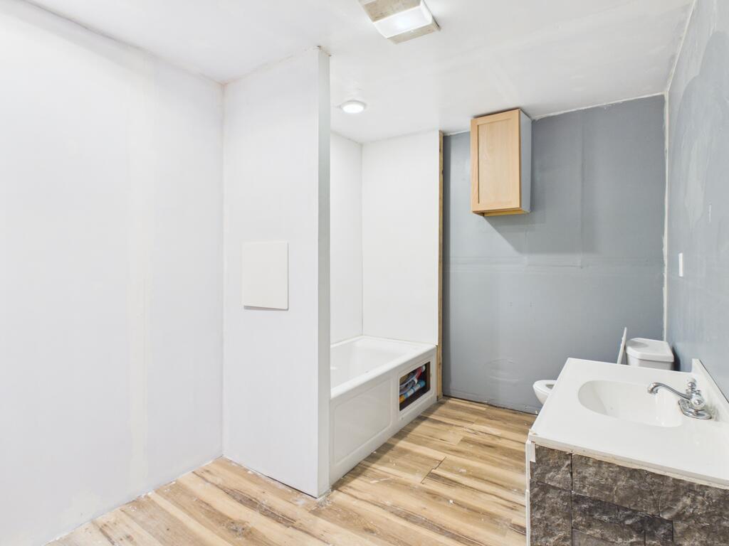 Bathroom with a bathtub, toilet, and sink vanity against gray walls and wood-look flooring.