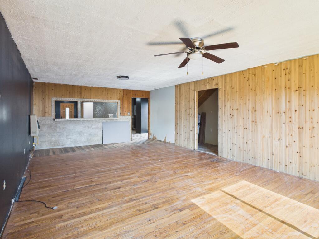 Empty room with hardwood floors, wood-paneled walls, and a stone-faced pass-through counter.