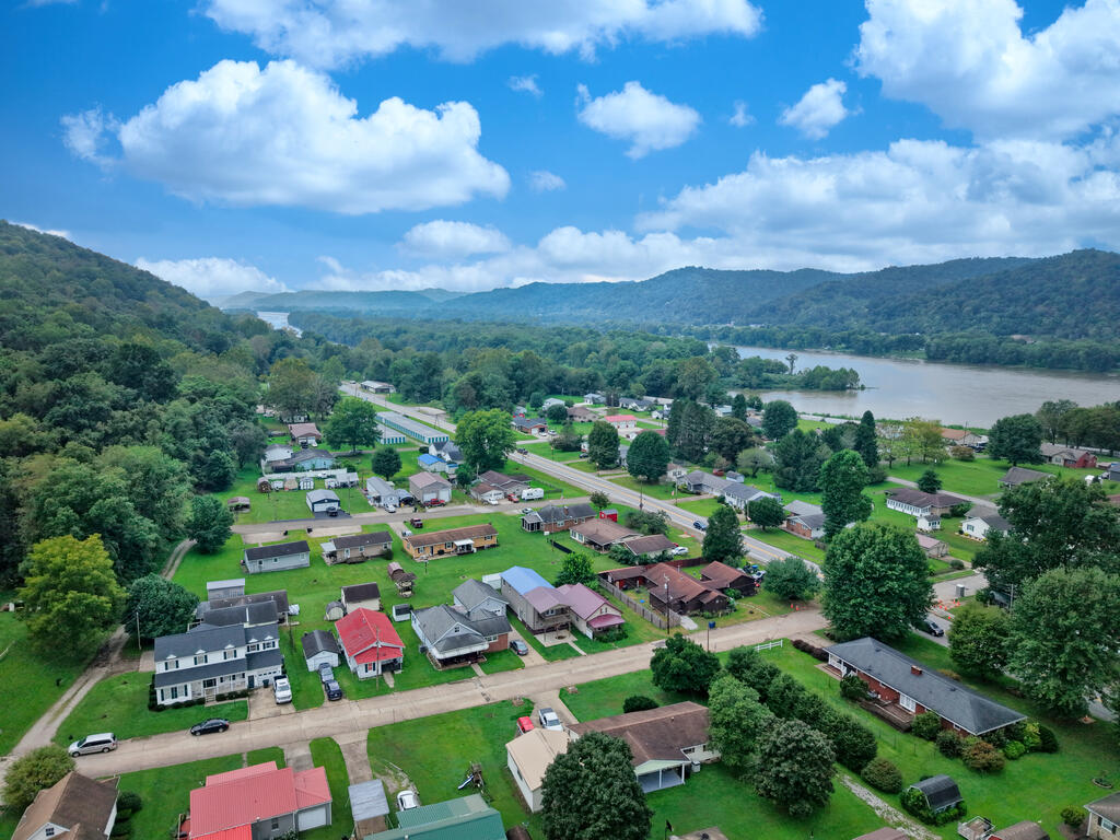 Aerial view of homes near a river, with wooded hills beyond.