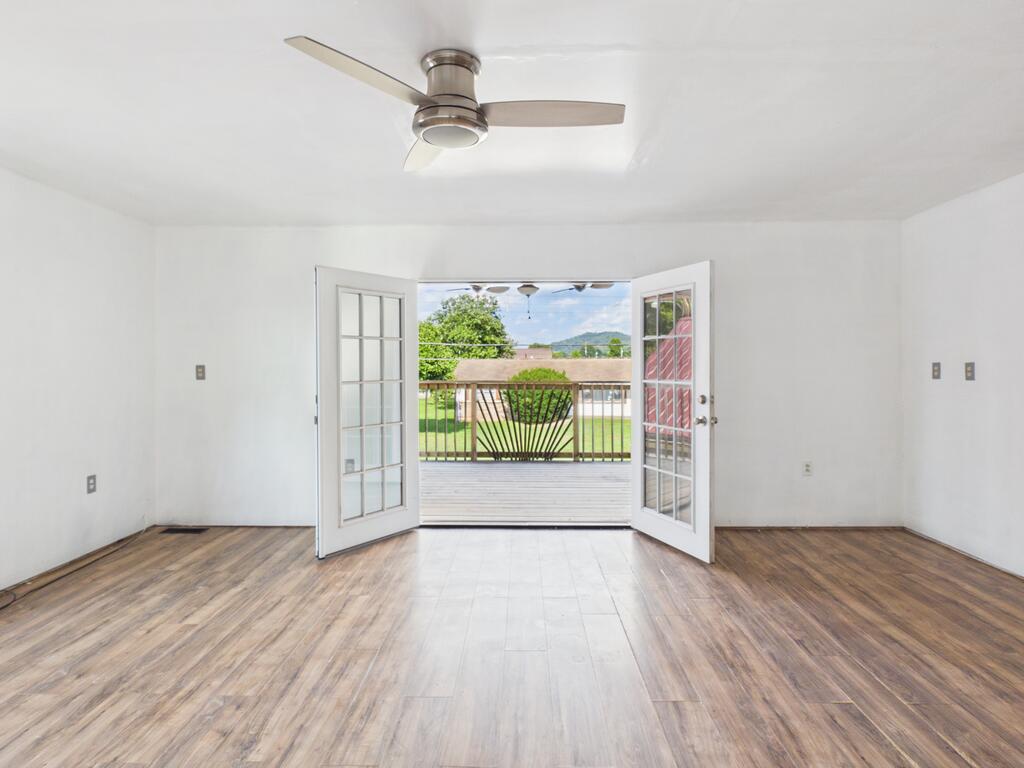Vacant room with wood-look flooring and open French doors leading to a deck.