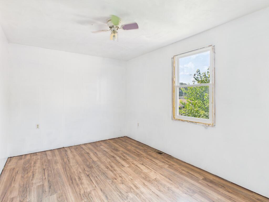Empty room with wood-look flooring, a ceiling fan, and a window overlooking greenery.