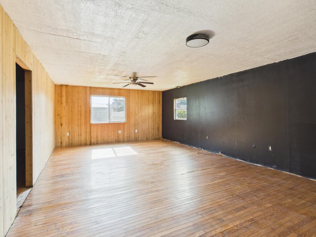 Empty living room with wood-paneled walls, a dark accent wall, and hardwood floors.