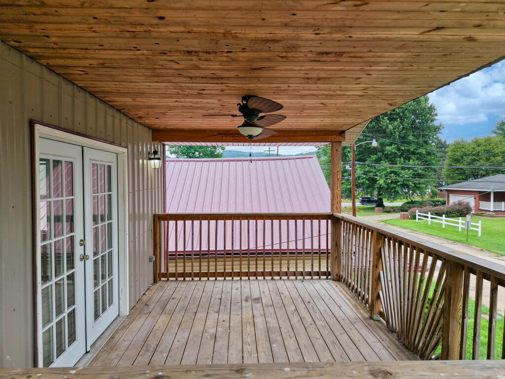 Covered wooden deck with a ceiling fan, French doors, and views of the residential street.