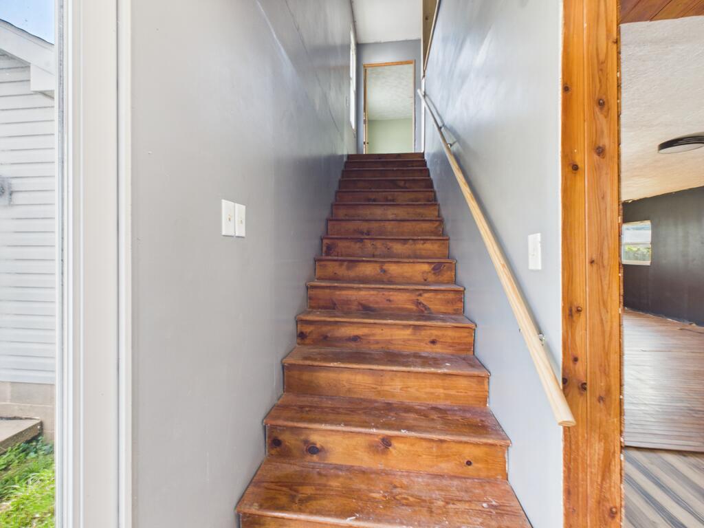 Worn wooden staircase rises between gray walls to an upstairs landing.