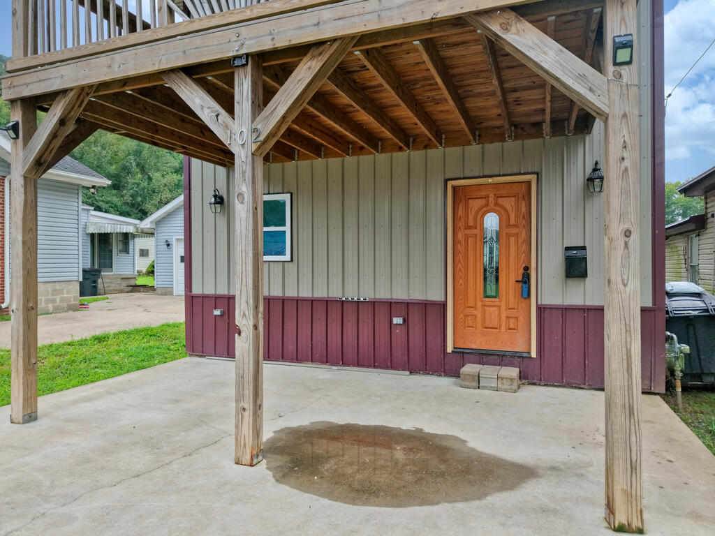 Front porch with exposed timber framing, a carved wooden door, and concrete slab.