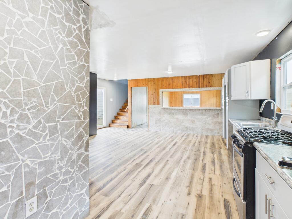 Open kitchen with white cabinets, gas range, wood-look floors, and a gray stone accent wall.