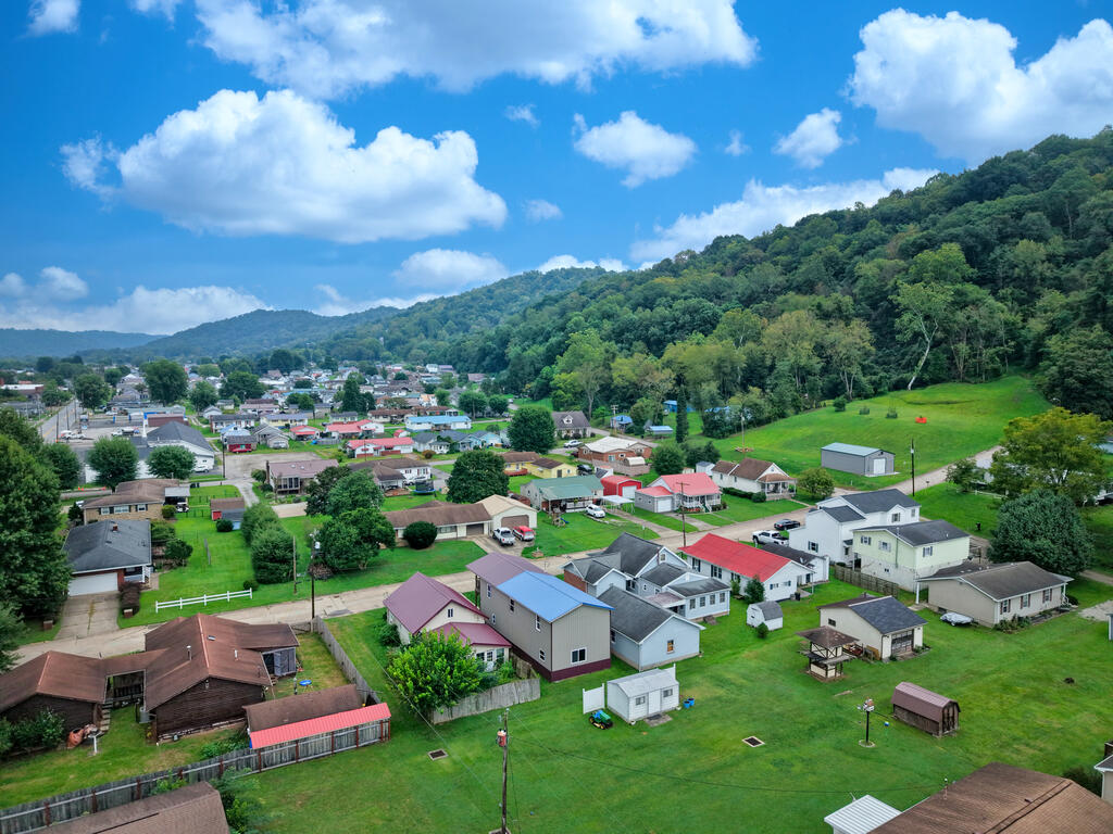 Aerial view of a small town beside wooded hills under a blue, cloudy sky.