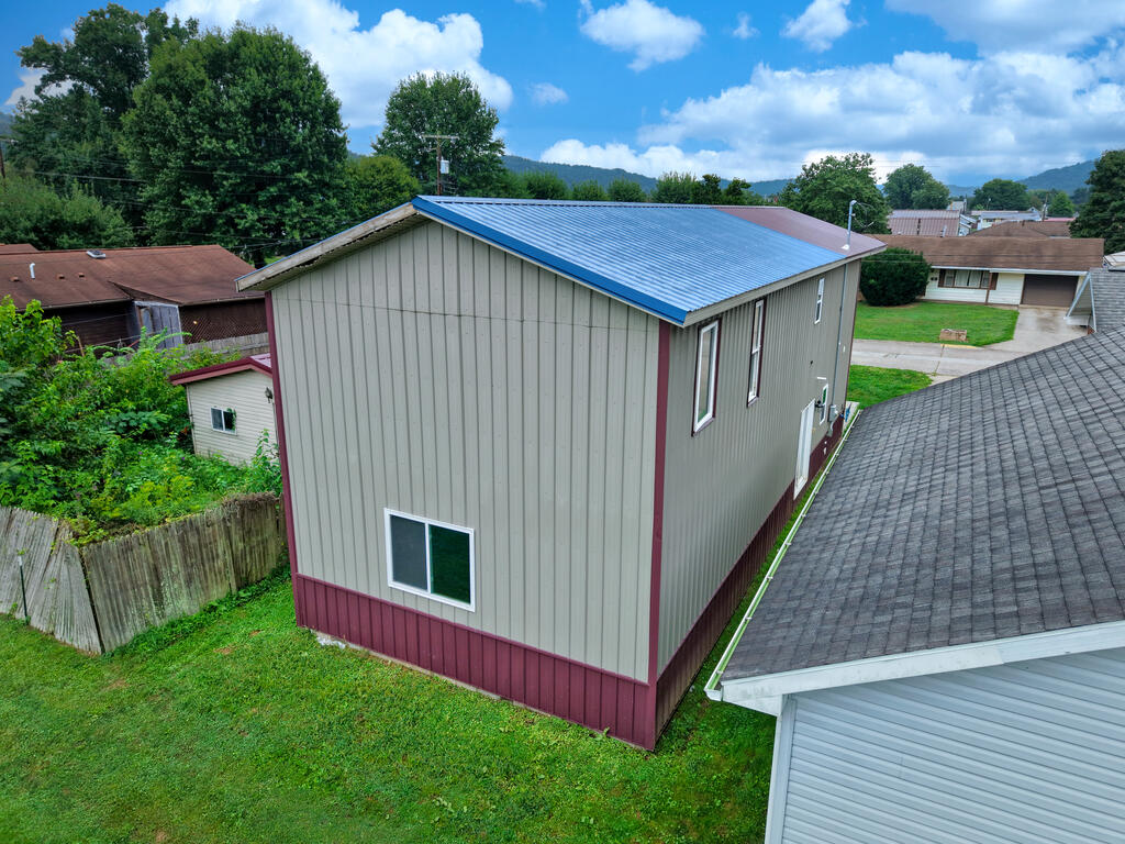 Narrow two-story building with a bright blue metal roof and light siding, viewed from above.