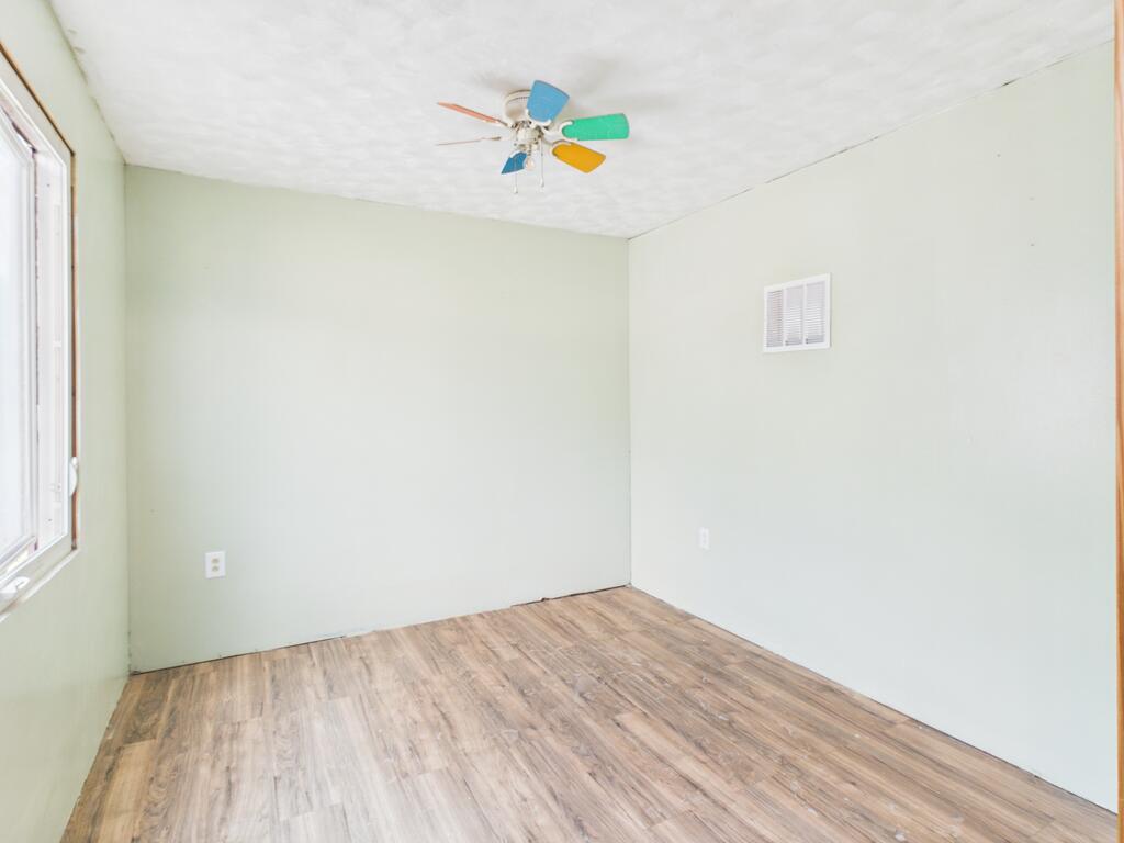 Empty room with wood-look flooring, a window, and a colorful ceiling fan.