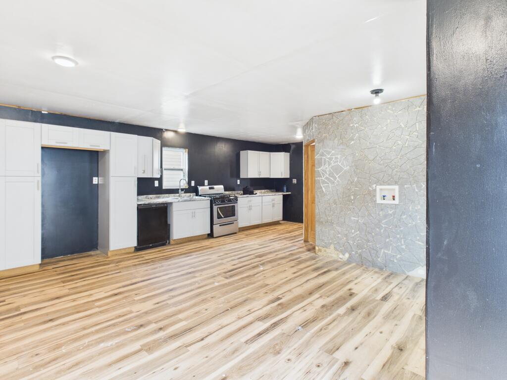 Unfurnished kitchen with white cabinets, stainless steel appliances, and wood-look plank flooring.
