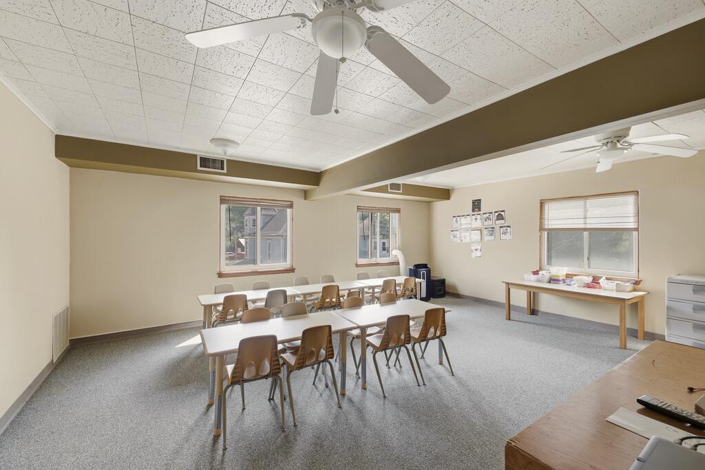 Classroom-style meeting room with rows of tables and chairs and windows along the back wall.