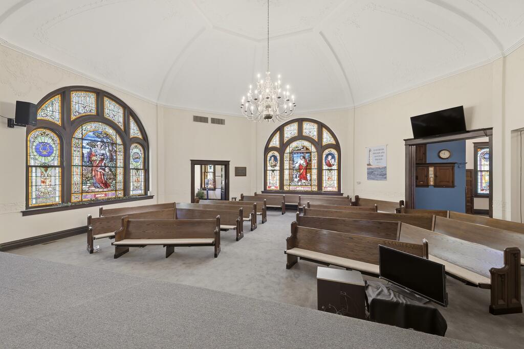 Chapel interior with wooden pews, large stained-glass windows, and a chandelier.