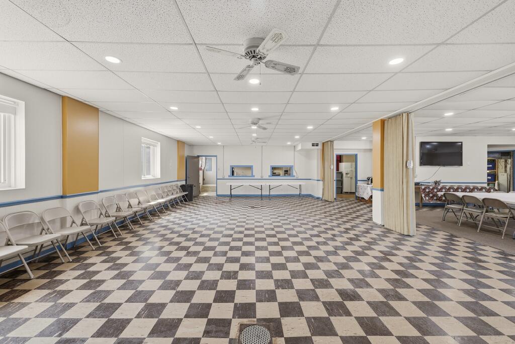 Large gathering room with checkerboard tile flooring, folding chairs, and curtains dividing the space.