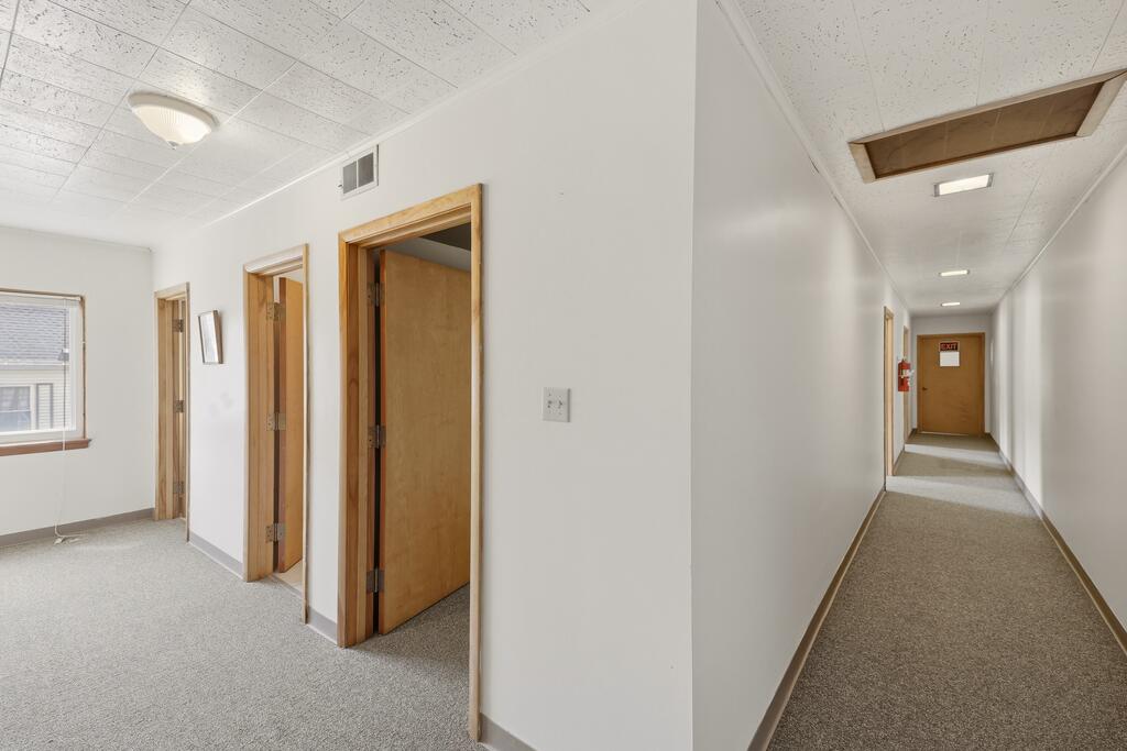 Carpeted hallway with several wood-trimmed doorways and an exit door at the far end.