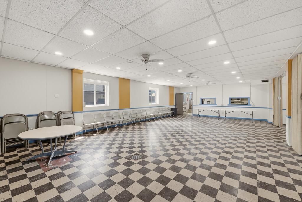Multipurpose room with checkerboard flooring, rows of chairs, and folding tables.