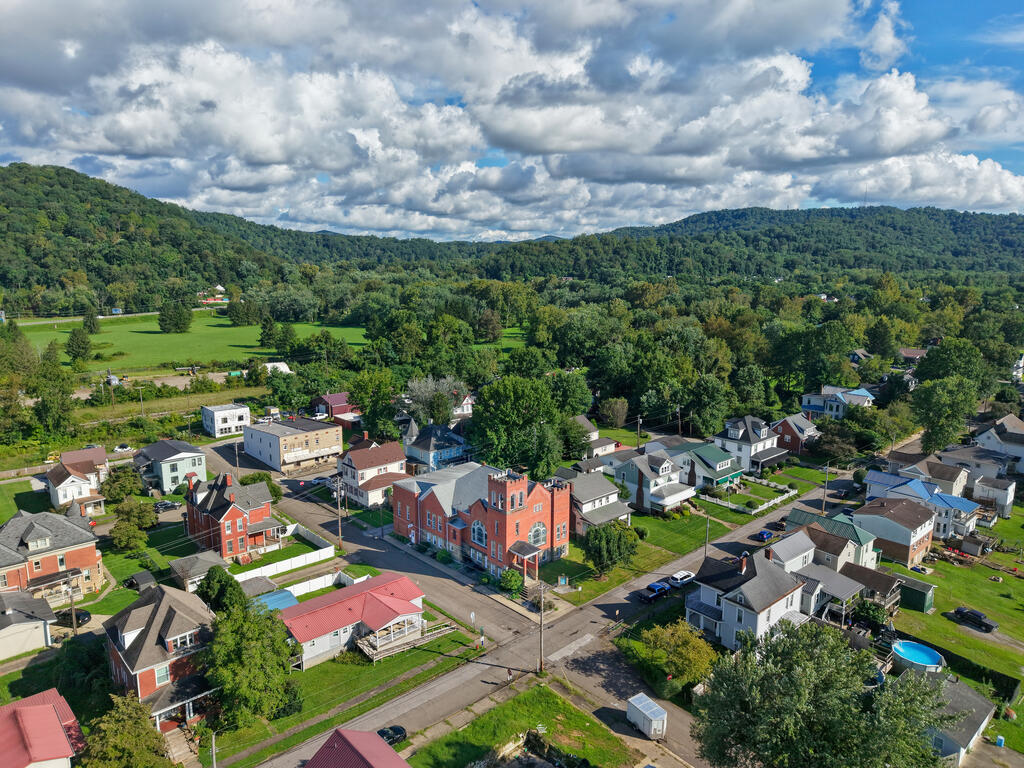 Aerial view of a small town nestled among wooded hills beneath a cloud-filled sky.