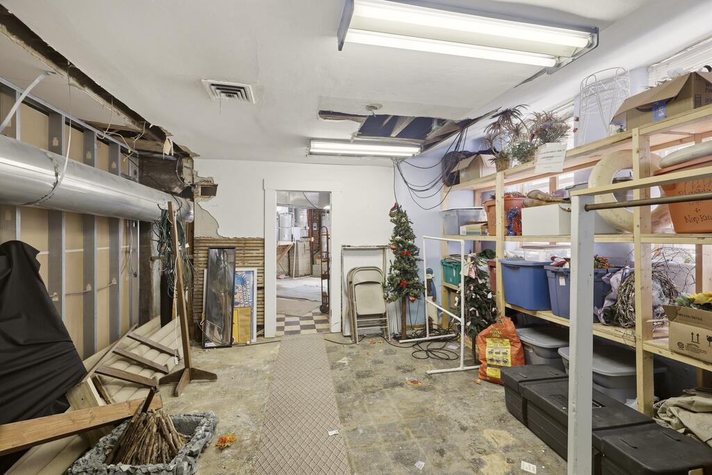 Storage room with packed shelves, exposed ceiling utilities, and a small decorated Christmas tree.