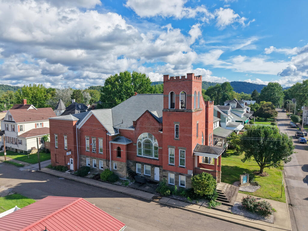 Red-brick building with a crenellated tower, viewed from above among neighboring homes and tree-lined streets.