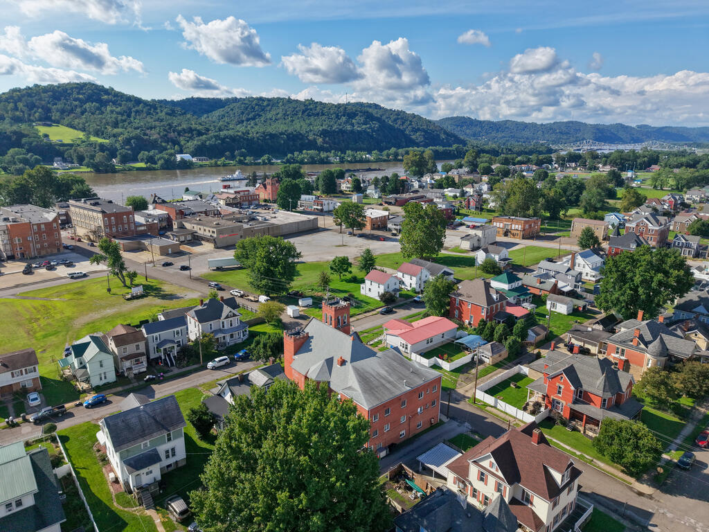 Aerial view of a riverside town, with wooded hills and a bridge beyond the neighborhood.