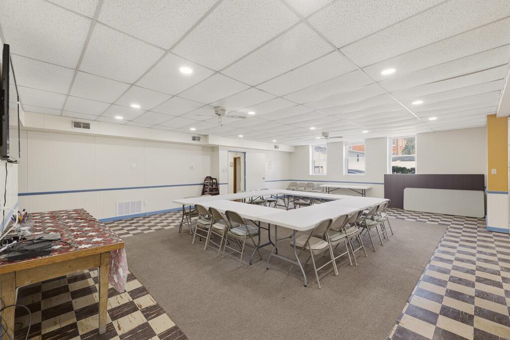 Large gathering room with folding tables, metal chairs, and a checkerboard floor.