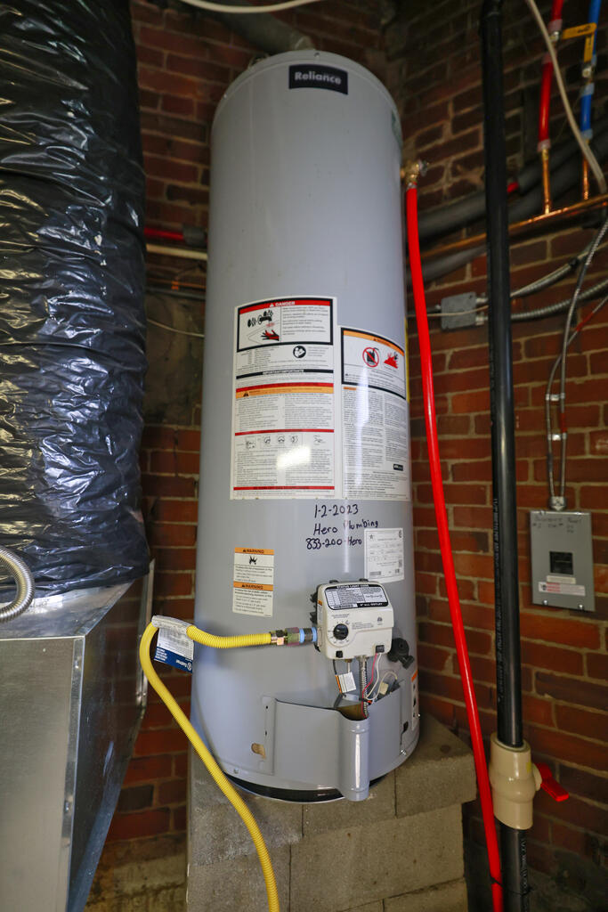 Reliance water heater in a brick basement, connected to a yellow gas line beside exposed ductwork.