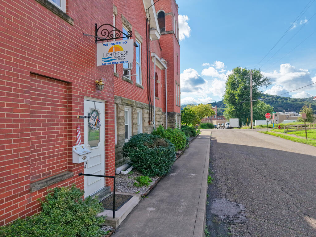 Red-brick building entrance with a Lighthouse Community sign and landscaped sidewalk.