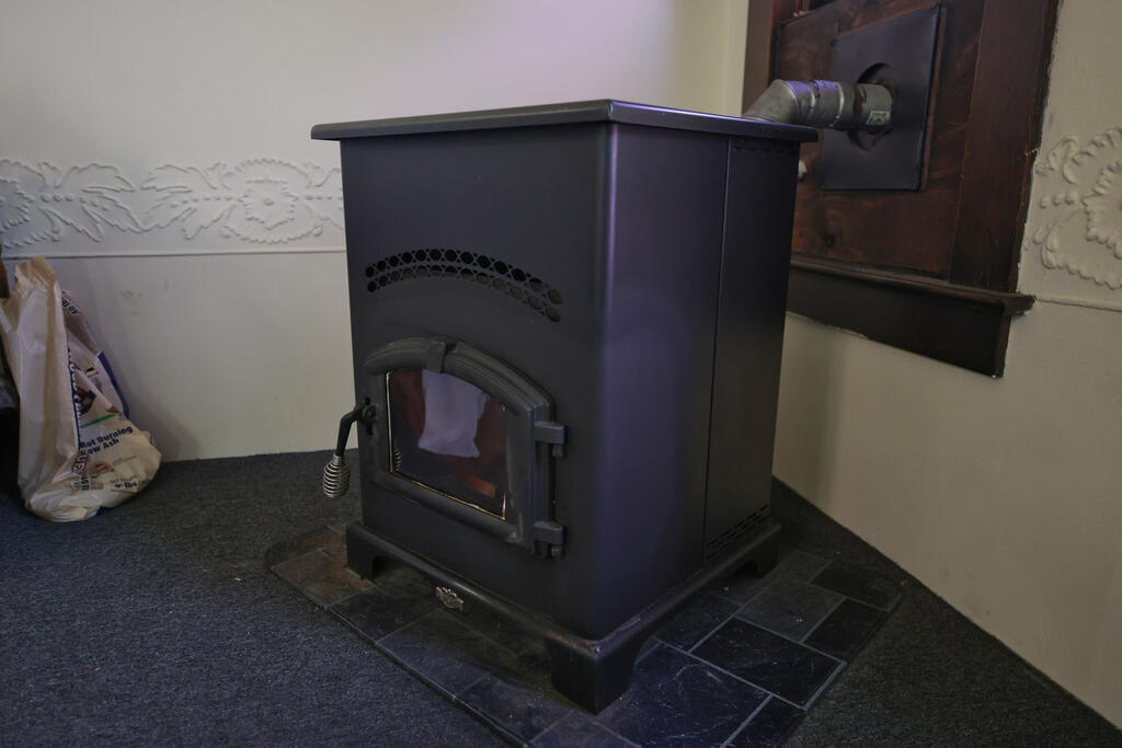 Black freestanding wood stove on a tiled hearth beneath embossed wallpaper.