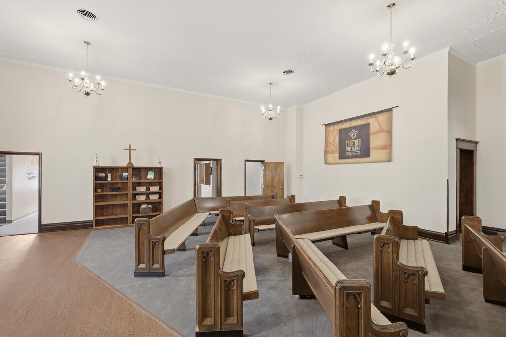 Chapel-like room with wooden pews, a cross-topped bookshelf, and chandeliers.
