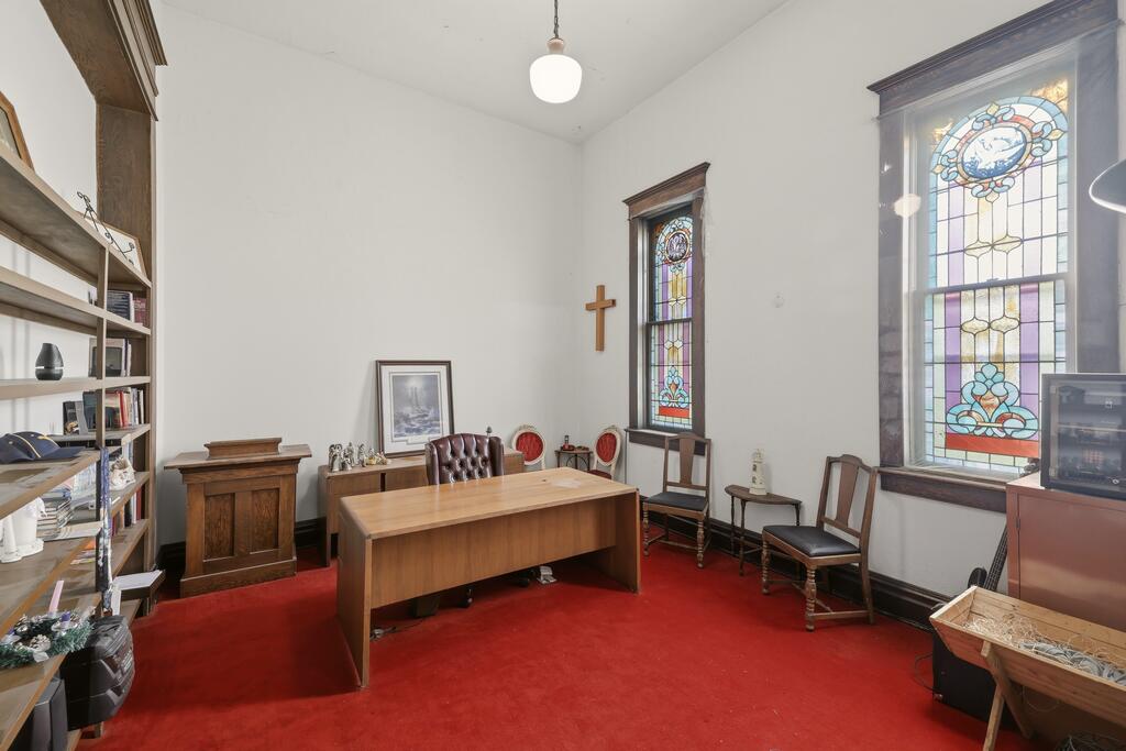 Interior room with a wooden desk, red carpet, stained-glass windows, and a wall cross.