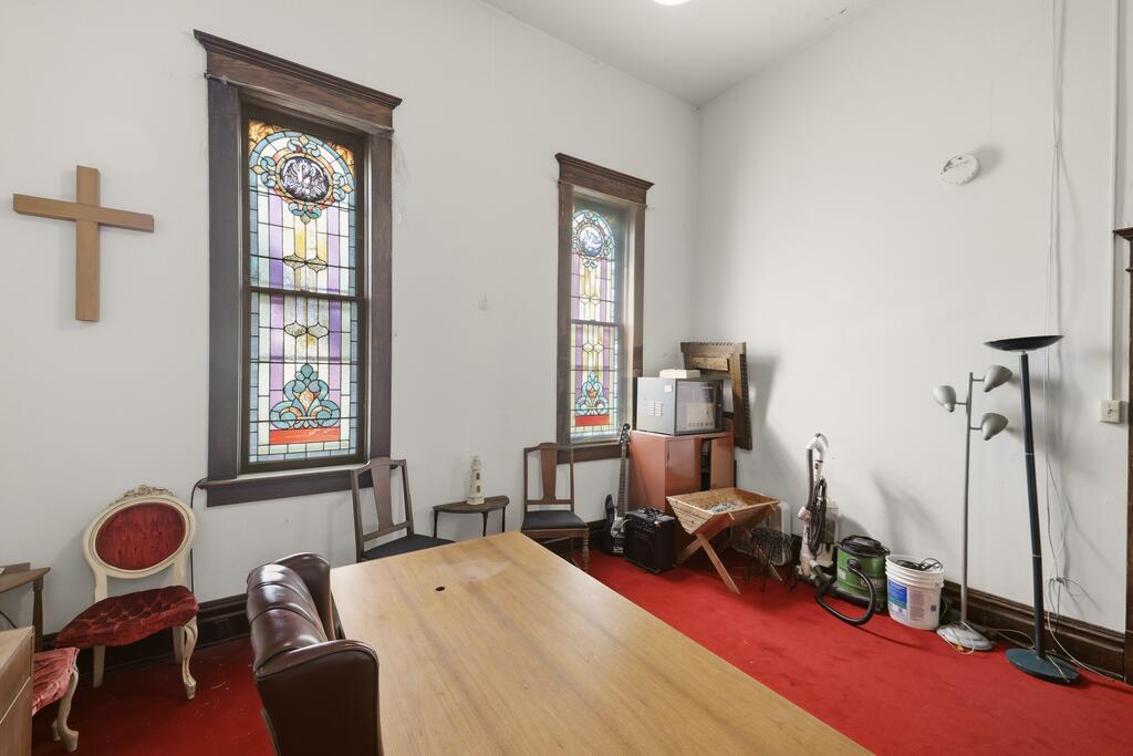 Room with stained-glass windows, a wooden cross, red carpet, and a large table.