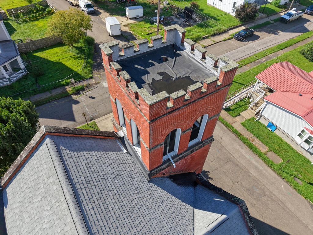 Aerial view of a red brick crenellated tower rising above gray shingle roofs.
