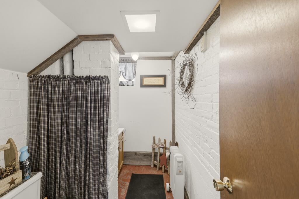 Narrow bathroom with a curtained shower alcove, white brick walls, and a wall-mounted heater.