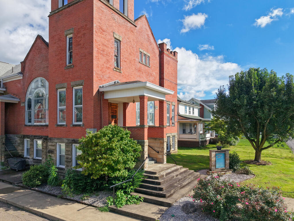 Red-brick building with an arched window, stone foundation, and landscaped front steps.