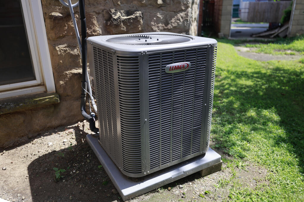 Lennox outdoor air-conditioning condenser beside a stone wall, on a concrete pad.