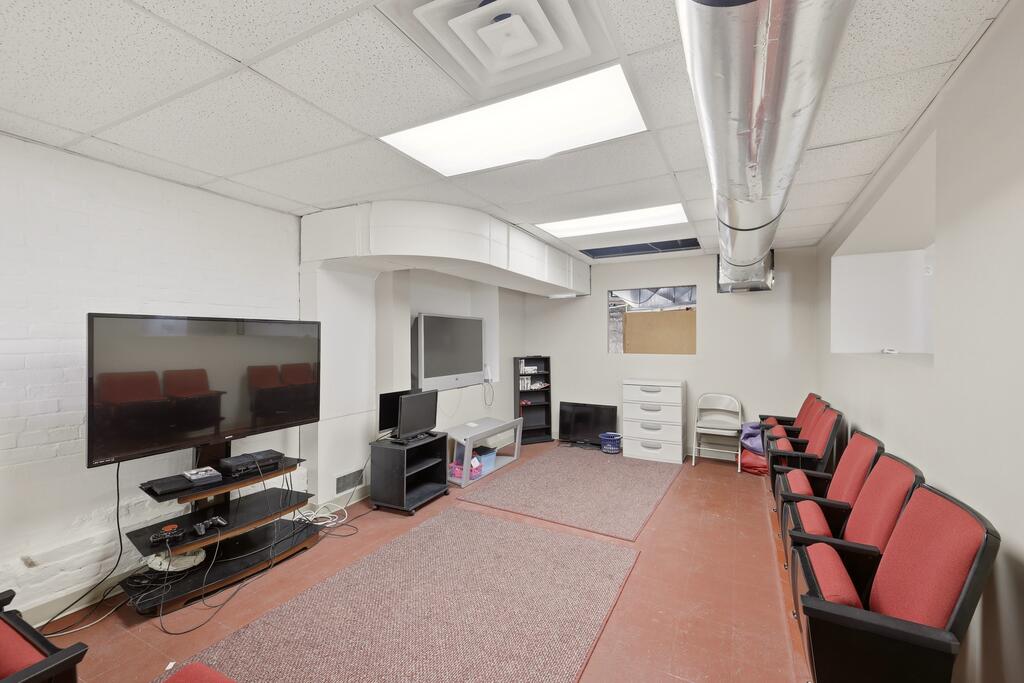 Interior room with red waiting chairs, two televisions, and exposed ceiling ductwork.