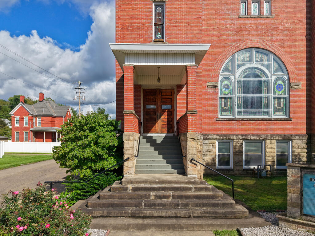 Red-brick building with a broad stone staircase, wooden entrance, and arched stained-glass window.