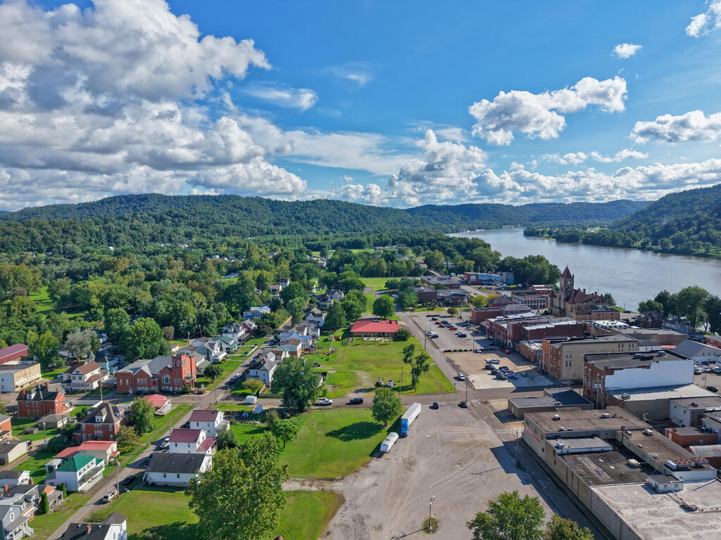 Aerial view of a riverside town with wooded hills and a broad river.
