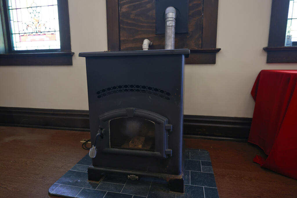 Black freestanding wood stove on a blue tiled hearth, with stained-glass windows behind it.