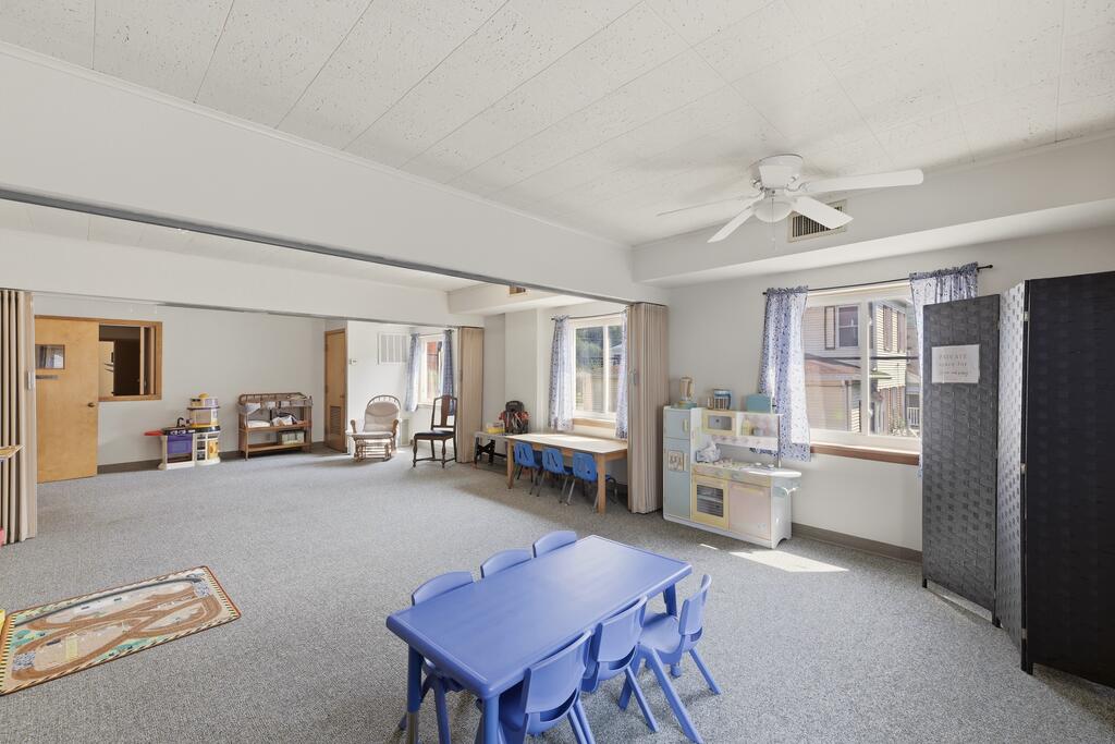 Spacious playroom with a blue children's table, toys, and windows with patterned curtains.