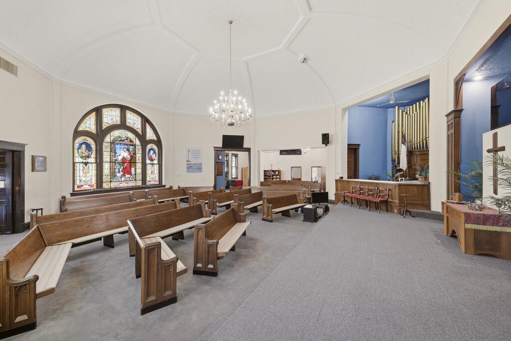 Church sanctuary with wooden pews, stained-glass window, chandelier, and pipe organ.