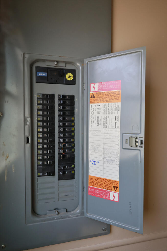 Open electrical breaker panel with rows of switches and safety labels on its door.