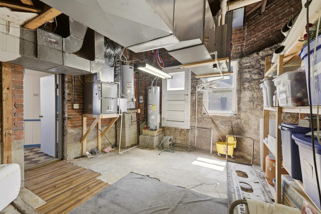 Unfinished basement utility room with exposed brick, mechanical equipment, storage shelves, and a concrete floor.