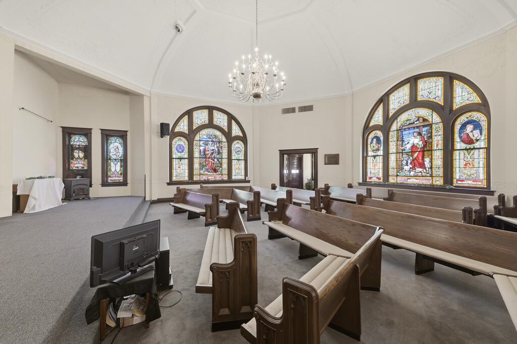 Chapel sanctuary with wooden pews, ornate stained-glass windows, and a chandelier.