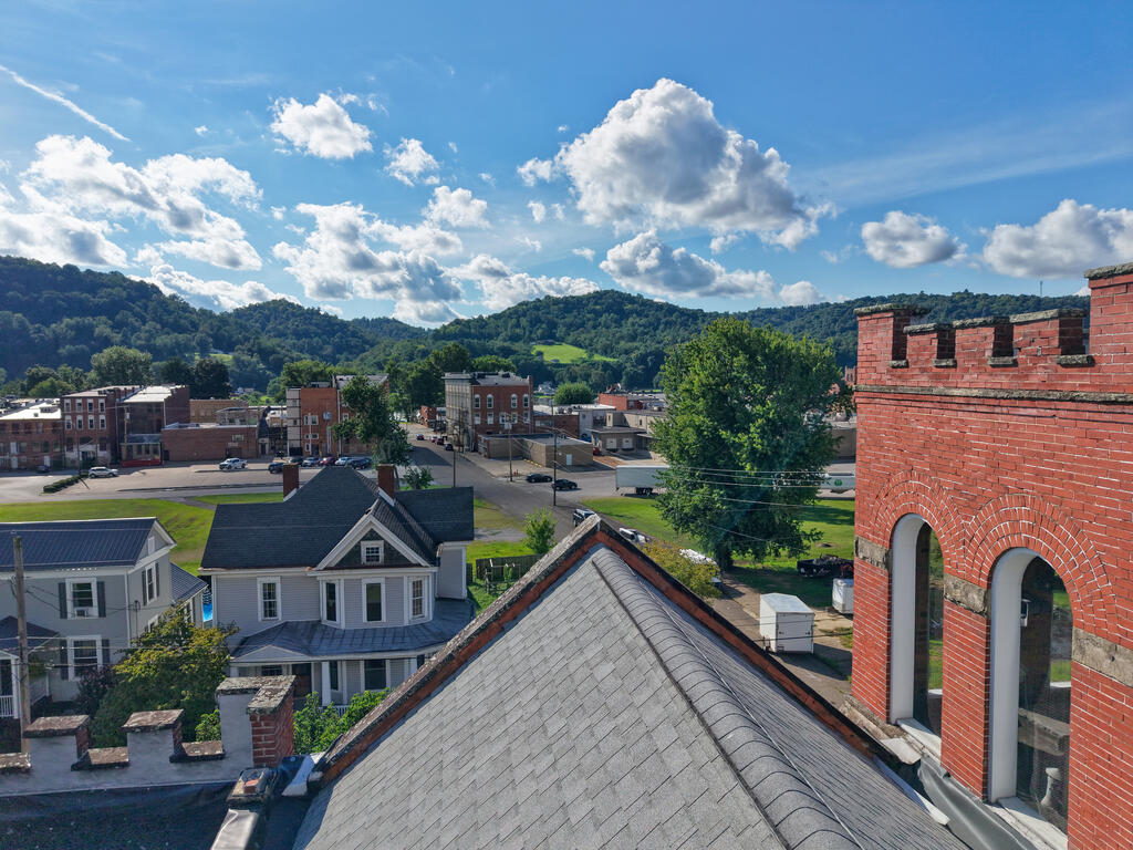 Elevated view over downtown rooftops toward wooded hills under a blue, cloud-filled sky.