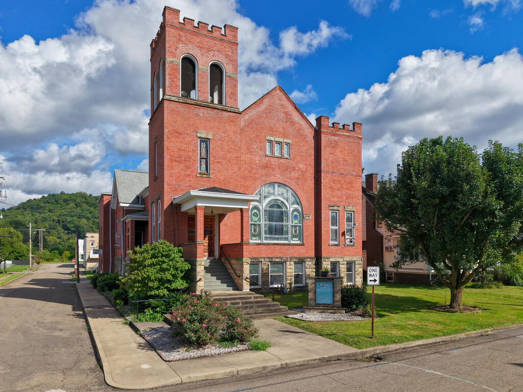 Red-brick building with a crenellated tower, arched stained-glass window, and landscaped lawn.