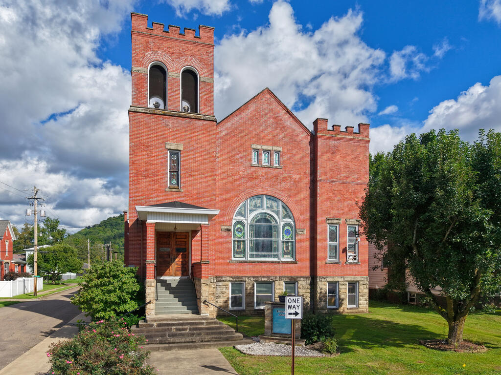 Red-brick building with a stone base, arched stained-glass window, and twin-opening tower.