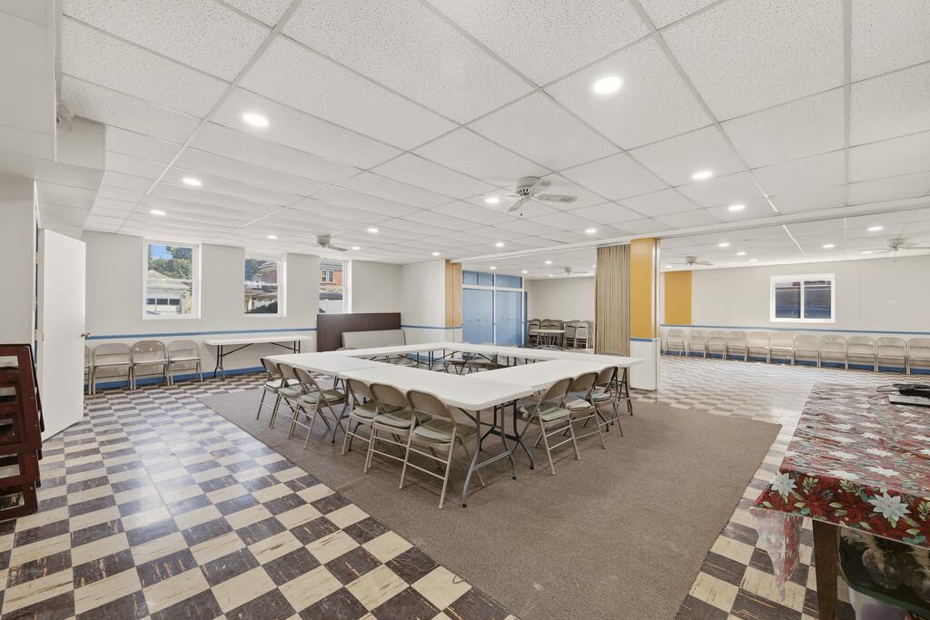 Meeting room with folding tables and chairs, checkered tile flooring, and a carpeted seating area.