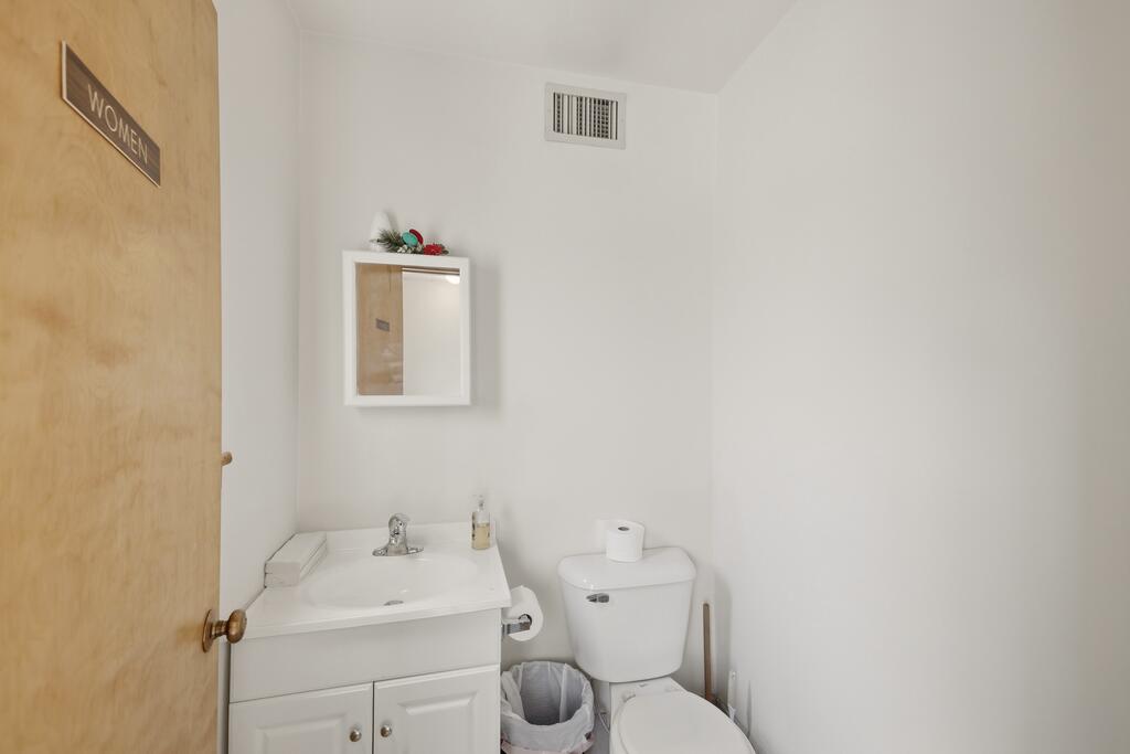 Bathroom with a white sink vanity and toilet beside a wooden door marked “WOMEN.”